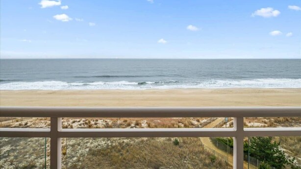 A beach view from a balcony with a railing, sandy beach, ocean, and sparse vegetation. - Two Bedroom Beachfront End Unit Condo with Pool. (Ocean City)