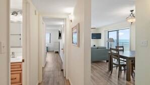 A hallway leading to a dining area with a view, a TV mounted on the wall, and a ceiling light fixture. - Two Bedroom Beachfront End Unit Condo with Pool. (Ocean City)