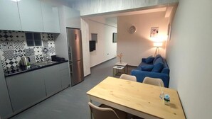 A compact kitchen with a refrigerator, a dining table with chairs, and a blue sofa in a small living area. - Ermou Junior Suite by Aesthetic & Luxurious Living (Athens)