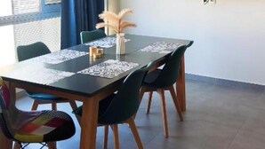 Un comedor con una mesa, sillas, un televisor de pantalla plana y un ventanal con cortinas.