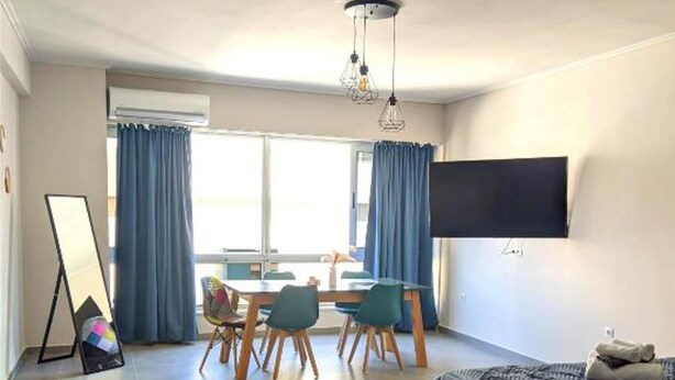 Una habitación de hotel moderna con una cama, un escritorio con sillas, un televisor de pantalla plana y un amplio ventanal con cortinas.