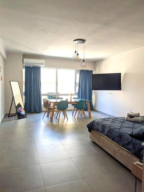 A modern hotel room with a bed, a desk with chairs, a flat-screen TV, and a large window with curtains. - Ermou Deluxe Suite by Aesthetic & Luxurious Living (Athens)