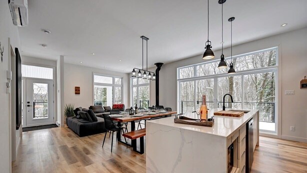 Ett rymligt kök med en central köksö, stora fönster och en matplats med soffa och stolar.