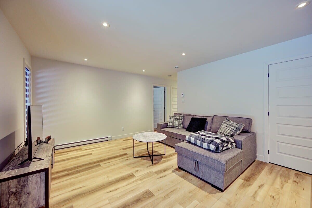 A modern living room with a grey sofa, a small round table, and a television on a wooden stand.