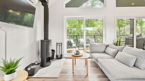 A modern living room with a large black wood stove, a grey sofa, and a TV mounted on the wall. - Le Sören - Sauna, Terrace, Fireplace & River (Sainte-Béatrix)