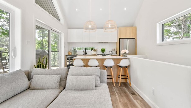 A modern kitchen with white cabinets, a central island with bar stools, and pendant lights. - Le Sören - Sauna, Terrace, Fireplace & River (Sainte-Béatrix)
