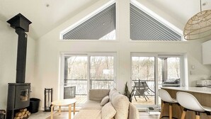 A spacious living room with a high ceiling, a fireplace, a sofa, and a dining area with chairs. - Le Sören - Sauna, Terrace, Fireplace & River (Sainte-Béatrix)