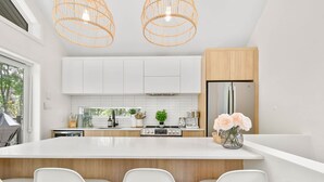 A modern kitchen with white cabinets, a large island with bar stools, a refrigerator, and two hanging wicker chandeliers. - Le Sören - Sauna, Terrace, Fireplace & River (Sainte-Béatrix)