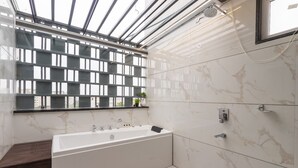 A modern bathroom with a bathtub, a shower, and a window with a metal grid. - JANKI PALACE (Bhopal)