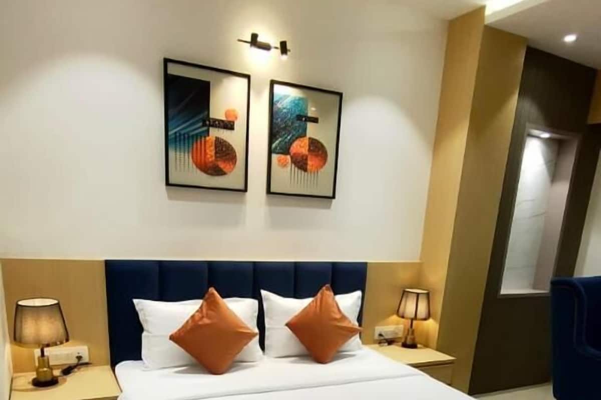 Quarto de hotel com uma cama grande, duas mesas de cabeceira, uma cabeceira azul e duas obras de arte penduradas na parede.