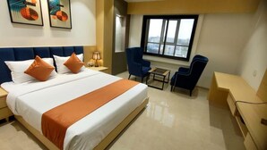 A hotel room with a large bed, two blue armchairs, a small table, and a window with a city view. - JANKI PALACE (Bhopal)
