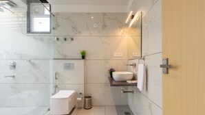 A modern bathroom with a glass shower enclosure, a toilet, a sink with a mirror, and a small plant on the countertop. - JANKI PALACE (Bhopal)