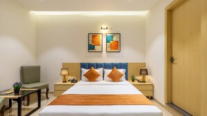A hotel room with a large bed, two nightstands, a chair, and a door. - JANKI PALACE (Bhopal)