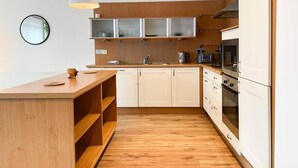 A modern kitchen with wooden cabinets, a central island, and built-in appliances. - Lovely Spacious Apartment with Hydro & SECC (Glasgow City)