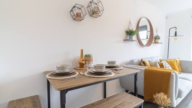 En matplats med ett träbord för fyra personer, en bänk och en soffa med kuddar.