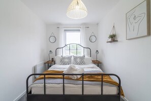 A neatly arranged bedroom with a bed, bedside tables, a hanging light fixture, a window with curtains, and wall art. - Luxury Glasgow flat in the heart of the West end (Glasgow City)