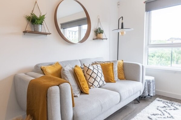 A modern living room with a grey sofa, mustard-colored throw, and patterned cushions. There are two wall-mounted planters and a floor lamp. - Luxury Glasgow flat in the heart of the West end (Glasgow City)