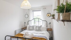 Ett välordnat sovrum med en säng, sängbord, en hängande lampa och ett fönster med gardiner.