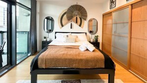 Un dormitorio moderno con una cama grande, dos mesitas de noche, un espejo amplio, un abanico decorativo y una puerta corredera de madera.
