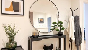 Un interior moderno con un espejo redondo, una consola decorada con objetos ornamentales, una planta en maceta y un perchero.