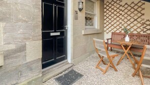 A building entrance with a black door, a window with a lattice design, and a wooden bench with a table. - Cozy 1 bed Blythswood Apartment (Glasgow City)