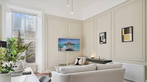 Una sala moderna con un sofá grande, una mesa de comedor y una planta en maceta. Hay un cuadro en la pared y una ventana con vistas al exterior.