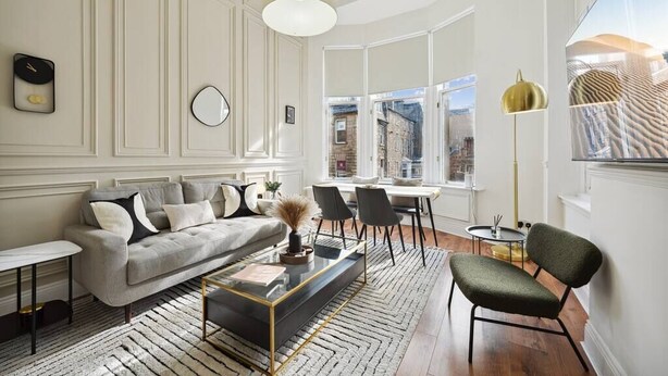 A modern living room with a sofa, coffee table, and chairs, a dining area with a table and chairs, and large windows offering a view of the city.