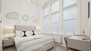 Un dormitorio moderno con una cama grande, mesitas de noche, un escritorio y una ventana con vidrio esmerilado.