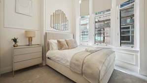 Un dormitorio con cama, mesita de noche, lámpara y vistas a un balcón con barandilla.