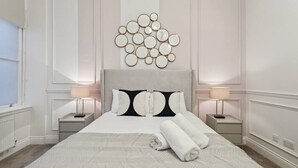 A hotel room with a large bed, two bedside tables with lamps, a wall clock, and a decorative wall piece. - (G5) Grand 1 bed Blythswood Apartment (Glasgow City)