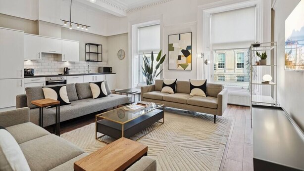 A modern living room with a sofa, coffee table, and a view of the city through large windows. - (G5) Grand 1 bed Blythswood Apartment (Glasgow City)