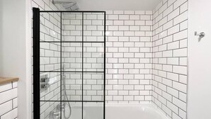 Ein Badezimmer mit weißen Fliesen im U-Bahn-Stil, einer Glasdusche und einer weißen Badewanne.