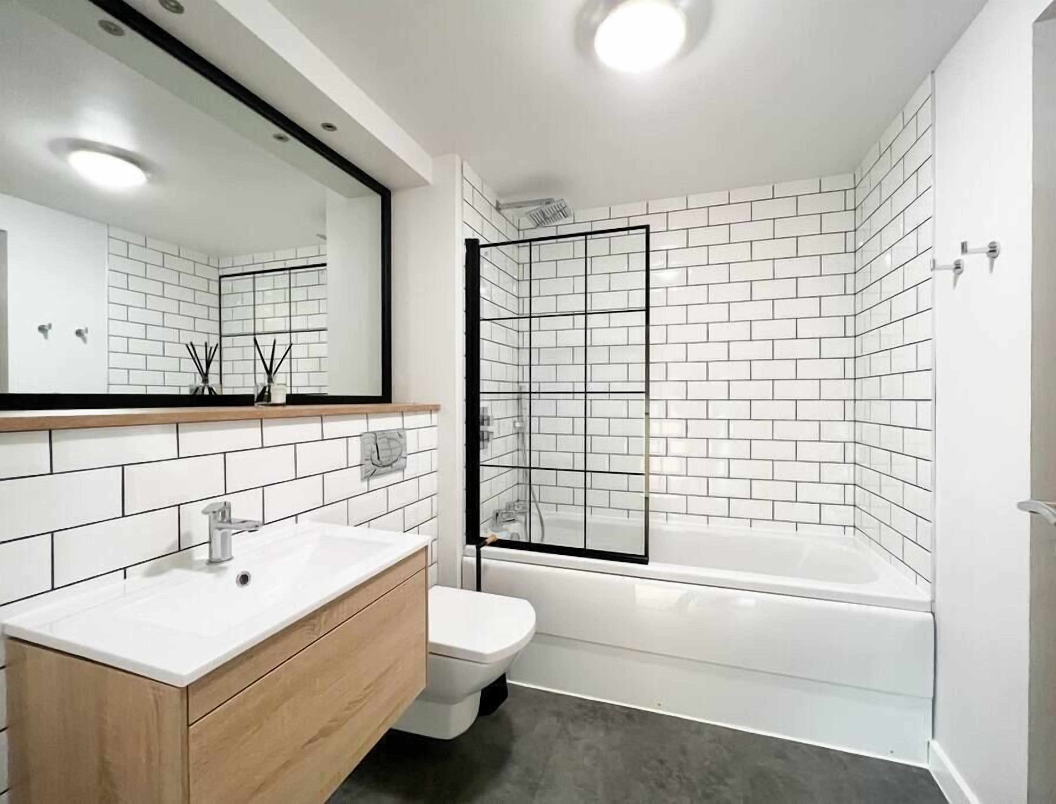A modern bathroom with a white sink, wooden vanity, a toilet, and a glass-enclosed shower area.