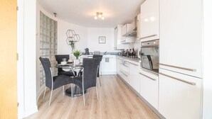 Een moderne keuken met witte kastjes, een eethoek met zwarte stoelen en een kleine tafel.