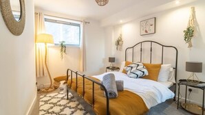 Een slaapkamer met een bed, nachtkastjes, een lamp, een spiegel en een raam.