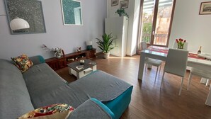 Een moderne woonkamer met een grijze bank, een eettafel met stoelen en een groot raam met zonwering.