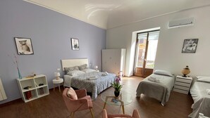 Een moderne hotelkamer met een groot bed, twee kleinere bedden, een zithoek met roze stoelen, een bijzettafeltje en een balkon met uitzicht.
