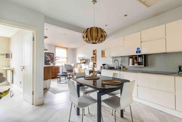 A modern kitchen with white cabinets, a dining area with a glass table and white chairs, and a hanging pendant light.