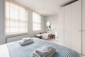 A bedroom with a bed, a large window, a bathroom with a bathtub, and a wardrobe.