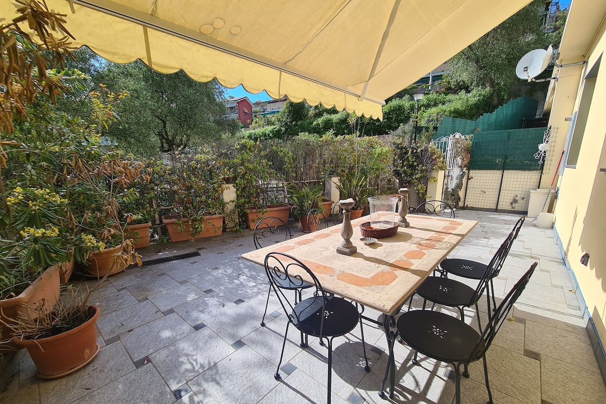 Eine Terrasse im Freien mit Fliesenboden, einem Tisch mit Stühlen und Blumentöpfen.