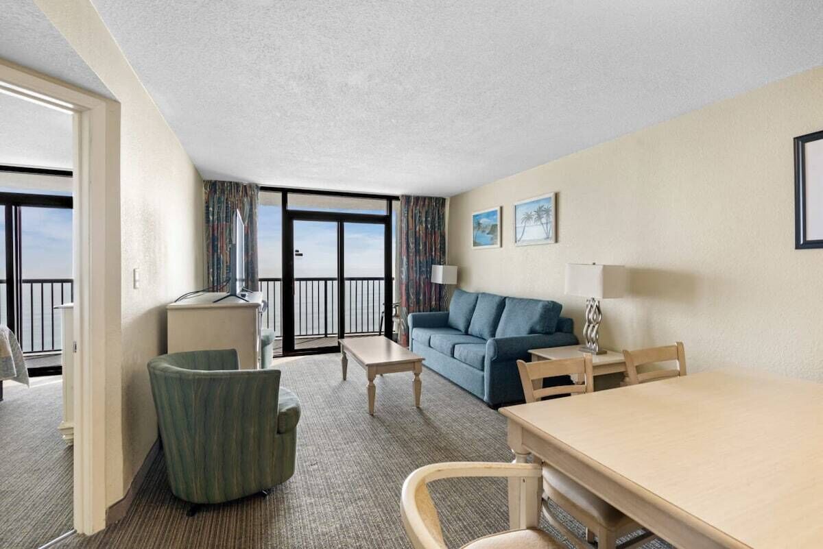 Habitación de hotel con balcón, sofá, mesa de comedor y una silla.