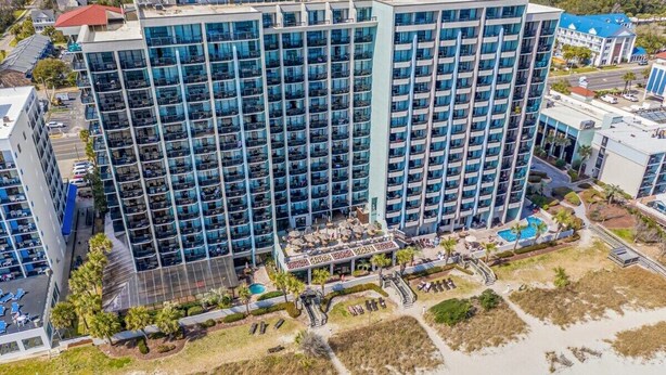 A high-rise hotel with multiple floors, a rooftop pool, and a landscaped area with palm trees.