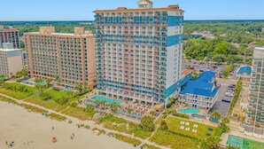 A high-rise hotel with multiple floors, a swimming pool, and a beach area.