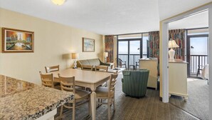 A hotel room with a dining area, a sofa, a small table, and a view of the sea through large windows. - Compass Cove Resort Unit 1216 - Oceanfront (Myrtle Beach)