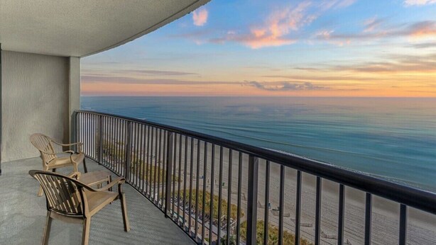 Un balcon avec deux chaises et une table, donnant sur une plage et l’océan.
