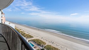 Une vue sur la plage depuis un balcon, avec une piscine et des chaises longues.