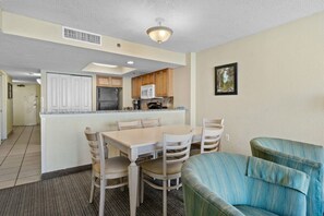 A compact kitchen with white cabinets, a microwave, and a refrigerator. There is a dining area with a table and chairs. - Compass Cove Resort Unit 1416 - Oceanfront (Myrtle Beach)