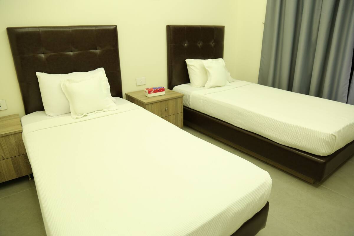 A hotel room with two single beds, wooden nightstands, and a small table with a box of tissues.