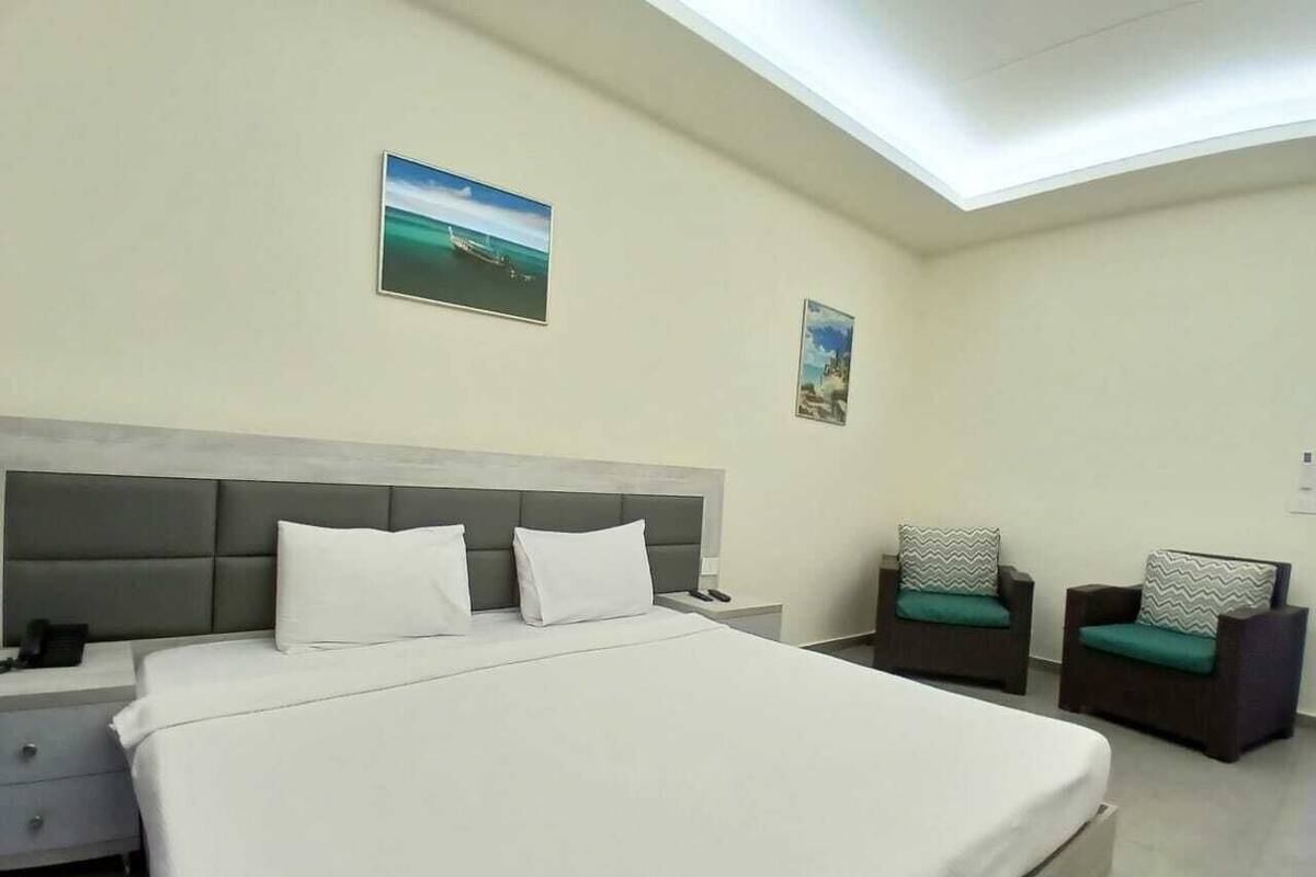 A hotel room with a large bed, a nightstand, two chairs, and two wall-mounted pictures.