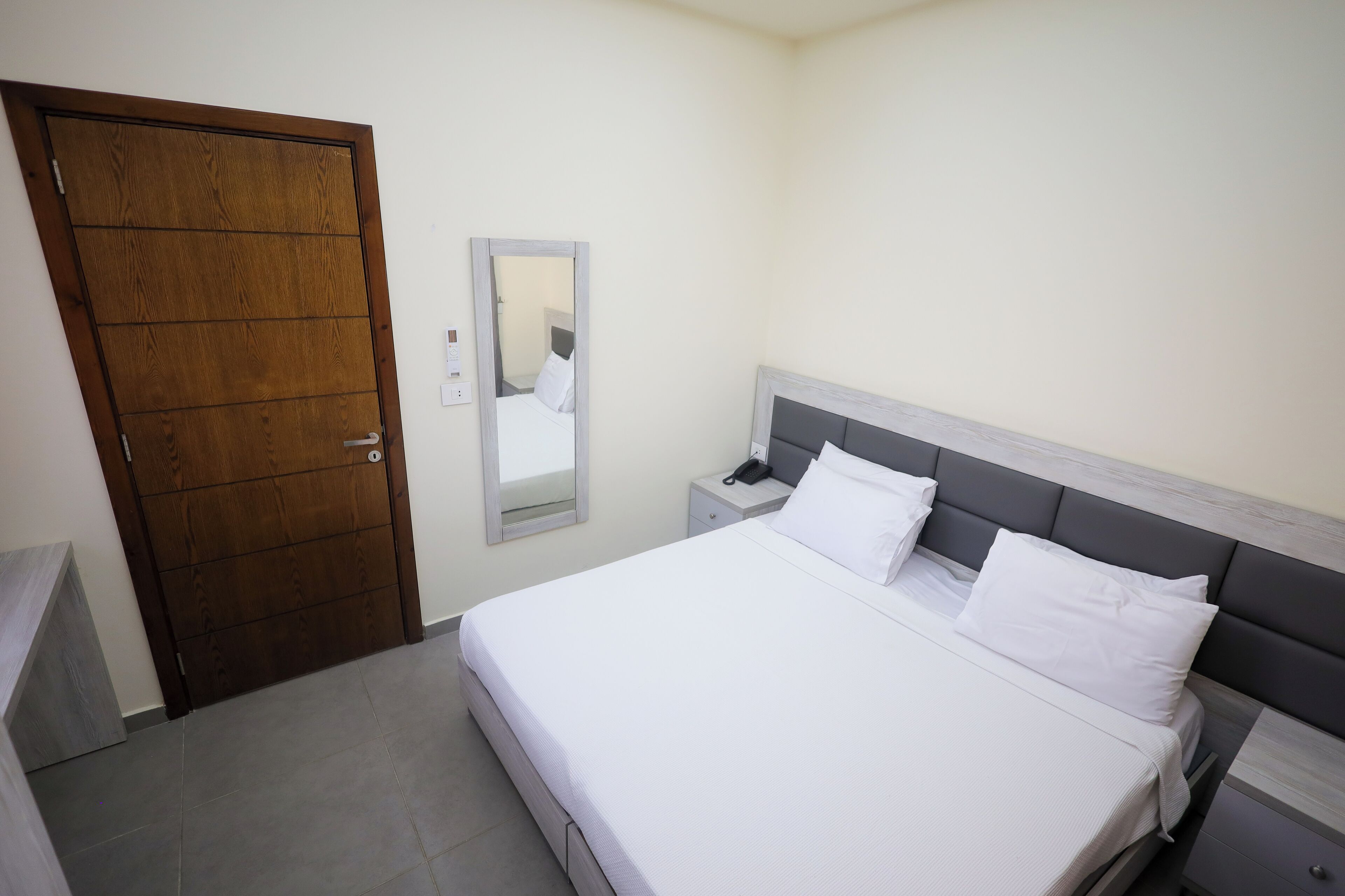 A bedroom with a wooden door, a bedside table with a phone, and a bed with white bedding.